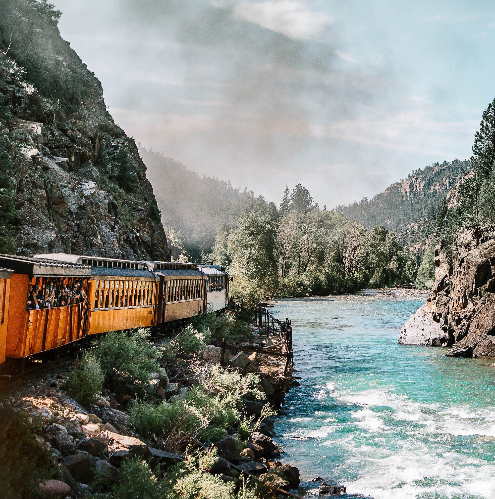 Train riding around the side of a mountain along the river