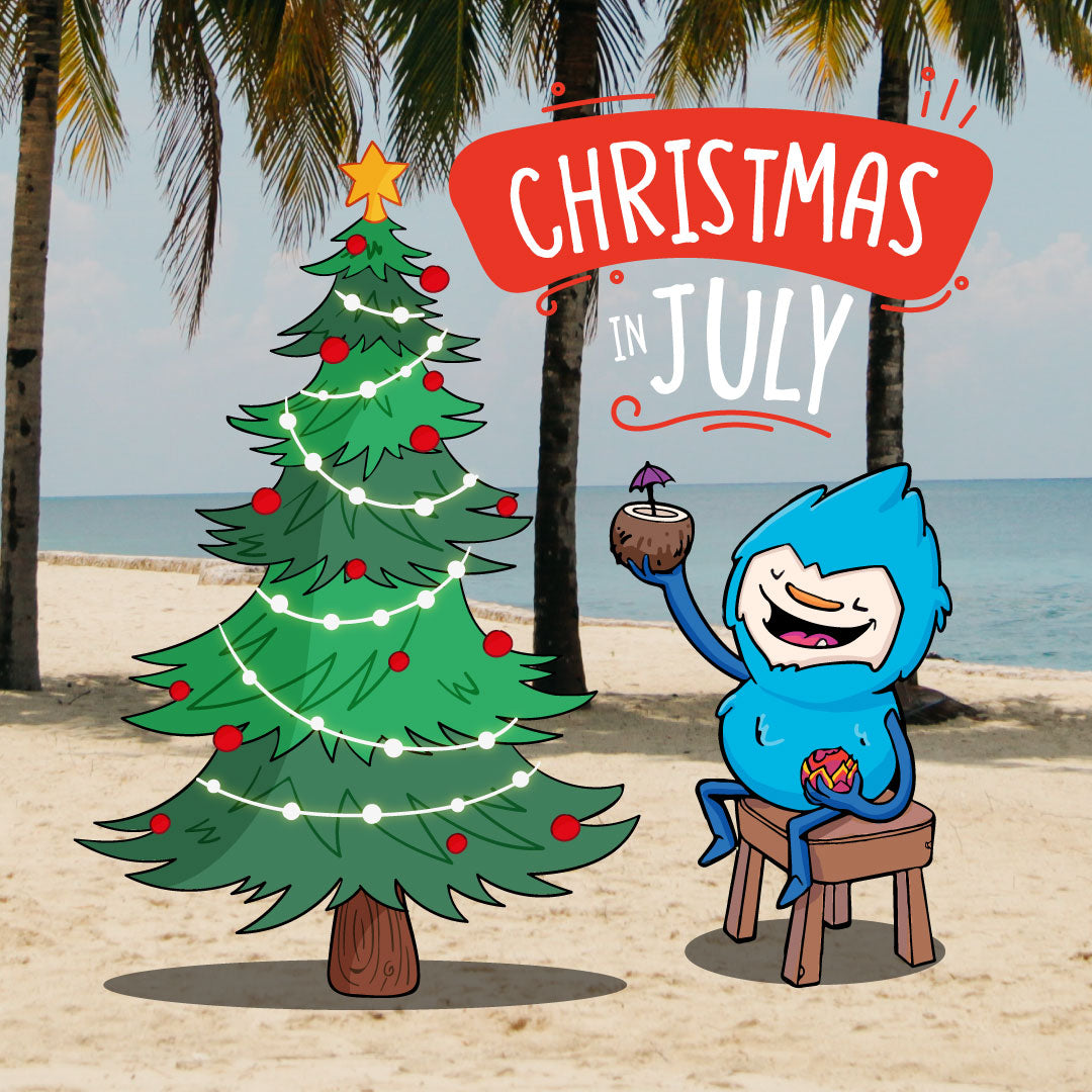 Womple enjoying Christmas in July on the beach with a drink in his hand in front of a Christmas tree