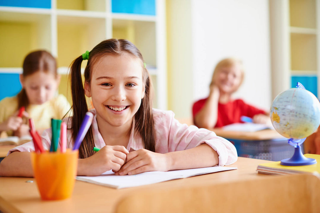 Smiling girl at her classroom desk with paper and pens