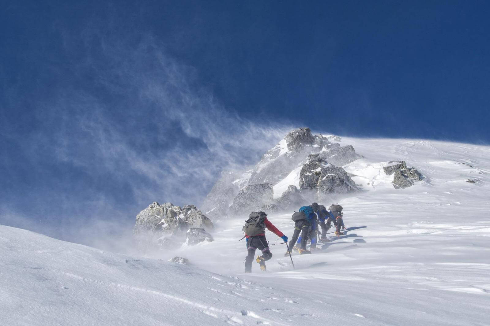 People hiking up a snow covered mountain in mountain snow gear