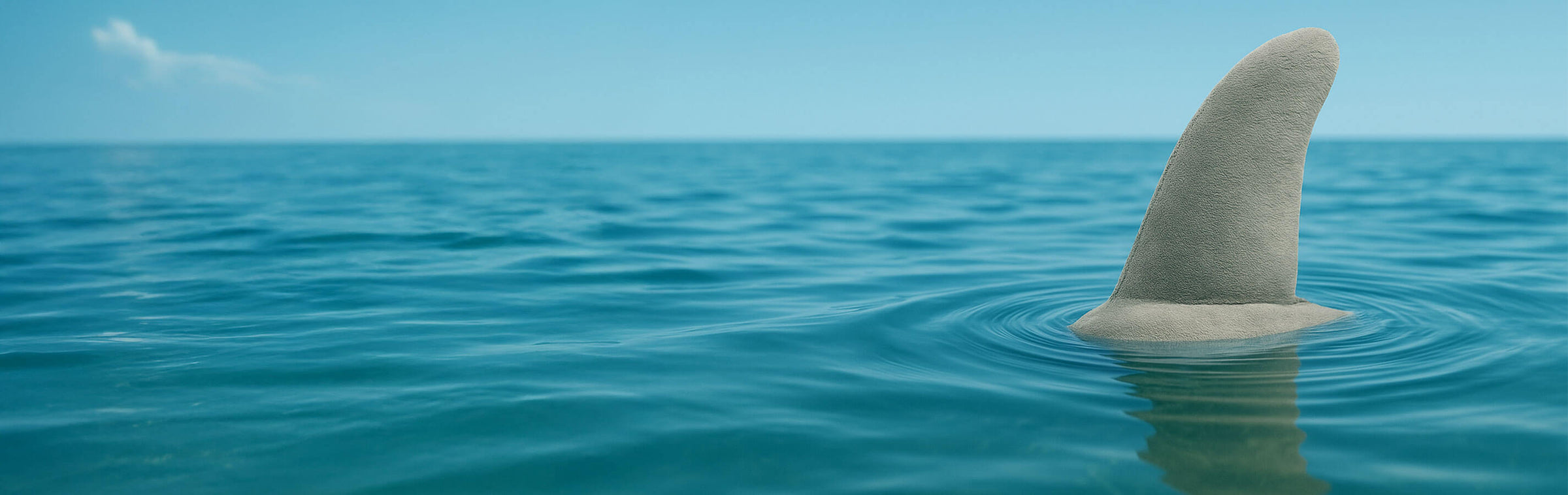 Shark fin emerging from the water with a clear blue sky