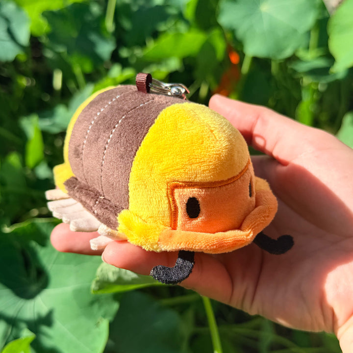 Plush rubber ducky isopod toy held in a hand with green leaves in the background