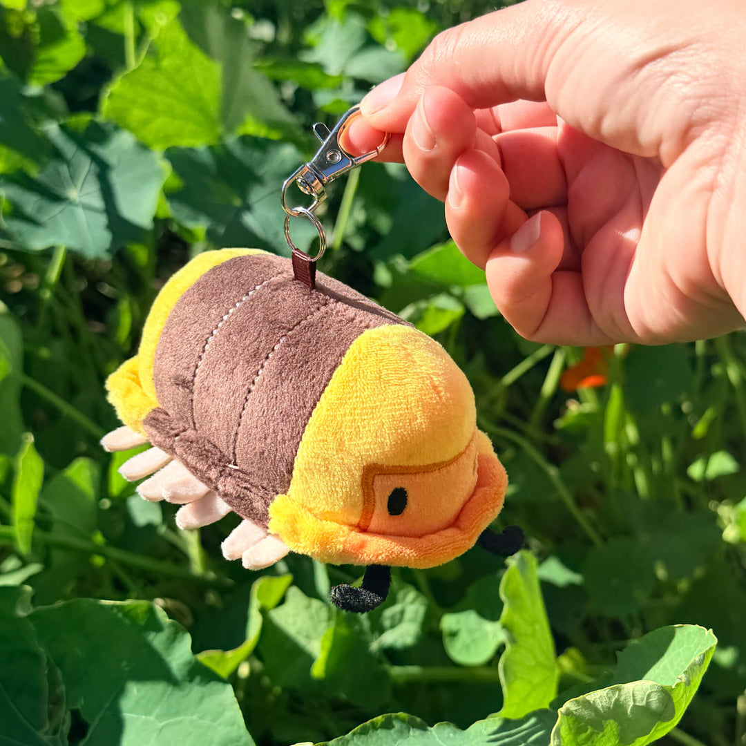 Plush rubber ducky isopod keychain toy held by a hand against a green leafy background