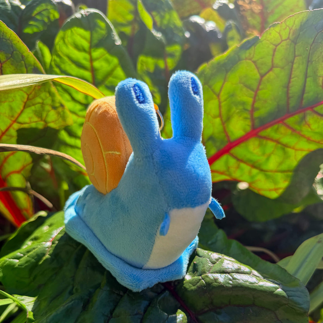 Blue plush toy snail keychain with a leafy garden background
