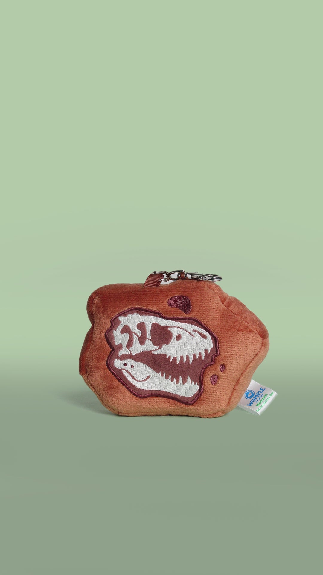 Rotating brown tyrannosaurus rex dinosaur fossil skull plush toy bag charm on a green background