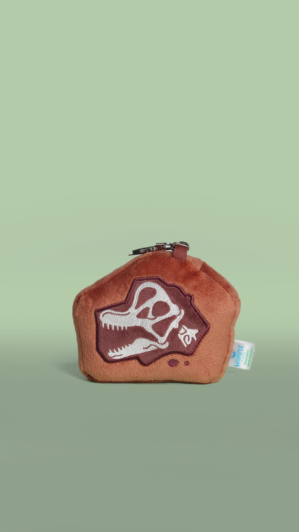 Rotating brown brachiosaurus dinosaur fossil skull plush toy bag charm on a green background
