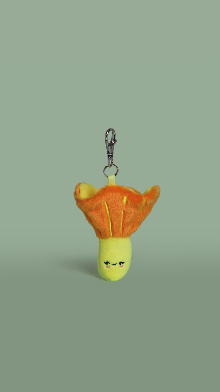 Rotation video of a plush toy golden chanterelle mushroom keychain with a face on a green background