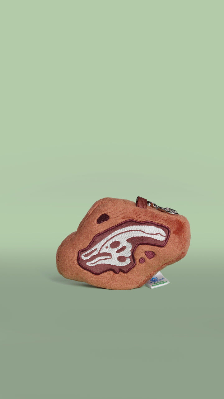 Brown plush bag charm with dinosaur fossil parasaurolophus skull design on a white background