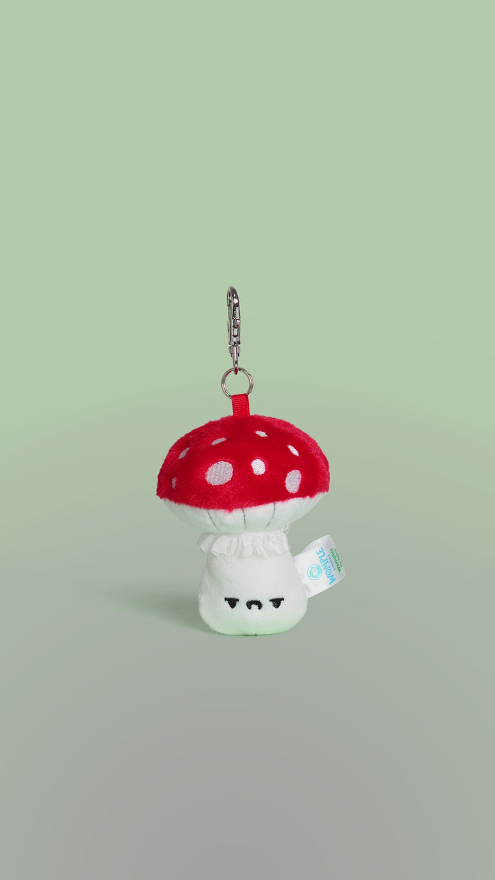 Rotating video of a plush toy fly agaric mushroom keychain with a face on a green background