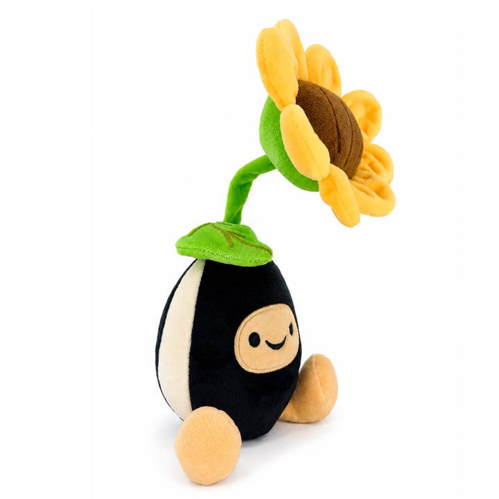 A plush toy shaped like a sunflower plant with a black and white seed body, tan face and feet, and a large yellow sunflower head with a brown center on a white background.