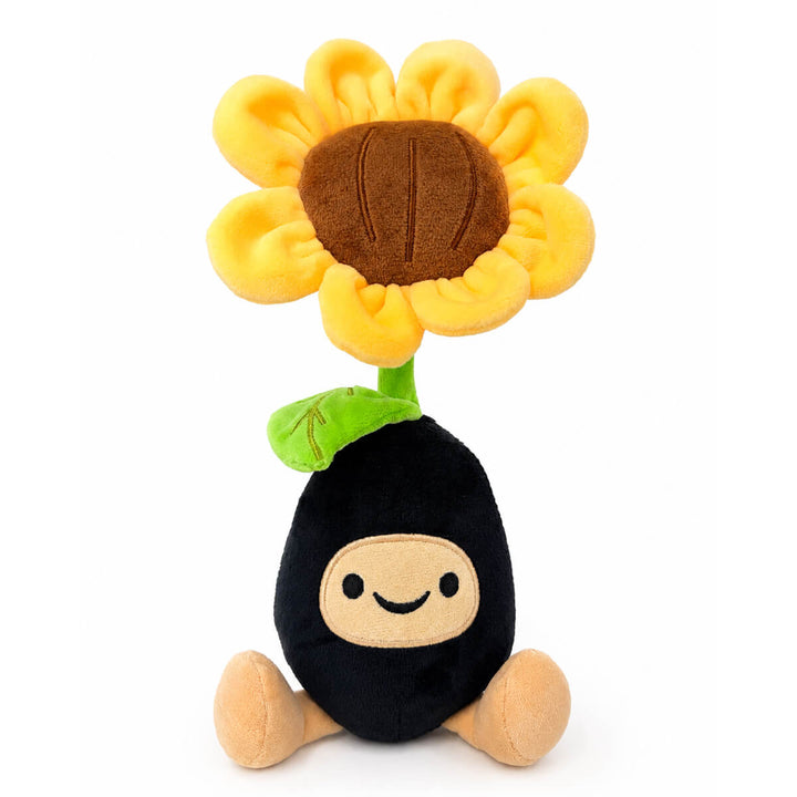 A plush toy shaped like a sunflower seed pod, featuring a black body, beige face and feet, a green stem, and a large yellow flower head with a brown center, set against a plain white background.