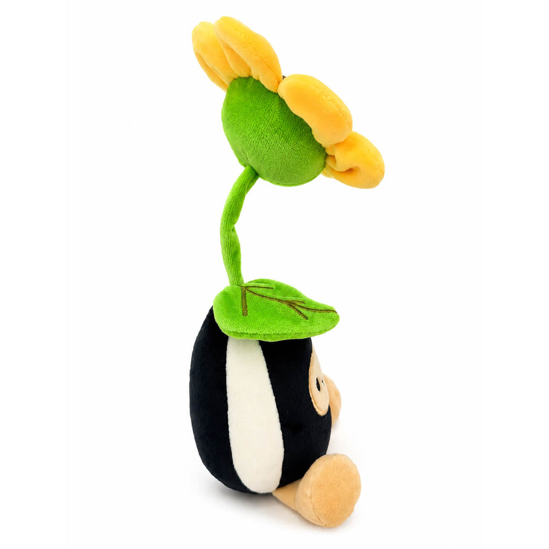 A plush toy featuring a sunflower seed body with black and white coloring, a tan face and foot, and a large yellow flower with a green stem and leaf on its head, photographed on a plain white background.